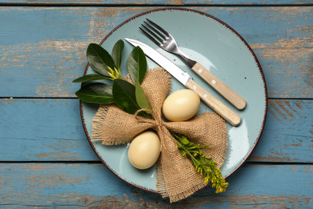 Stylish table setting with Easter eggs, napkin and cutlery on blue wooden background