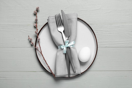 Beautiful festive table setting for Easter with egg and willow branch on light wooden background