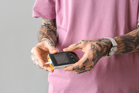 Diabetic young man using glucometer on light background