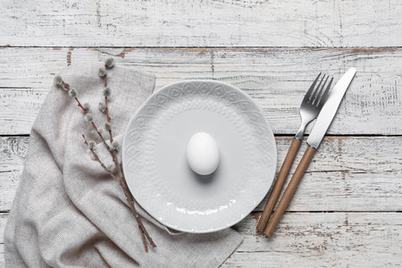 Beautiful festive table setting for Easter with egg and willow branch on light wooden backgroundの写真素材