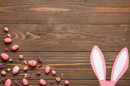 Painted Easter eggs with flowers and paper bunny ears on wooden background