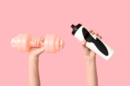 Female hands with dumbbell and bottle of water on pink background, closeupの写真素材
