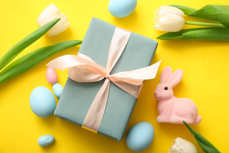 Easter eggs, tulip flowers with gift box and bunny on yellow backgroundの写真素材