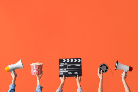 Many hands with bucket of popcorn, movie clapper and megaphones on orange backgroundの写真素材