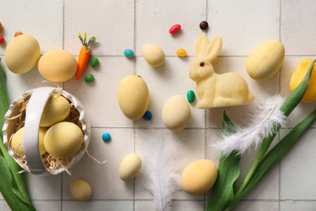 Ceramic basket with painted Easter eggs, tulip flowers and bunny on white tile backgroundの写真素材