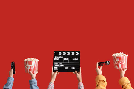 Many hands with movie clapper, buckets of popcorn and TV remote on red backgroundの写真素材