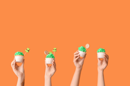 Female hands with tasty cupcakes for St. Patrick's Day on orange backgroundの写真素材