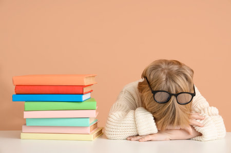 Tired little boy lying on table with books against color wallの写真素材