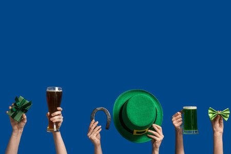 Female hands holding beer and party decor for St. Patrick's Day celebration on blue backgroundの写真素材