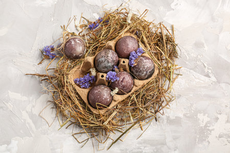Easter eggs in package with flowers and straw on gray grunge background