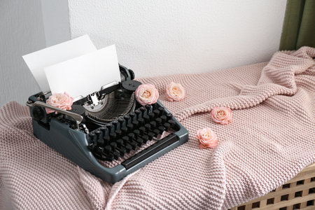 Vintage typewriter with paper sheet, knitted blanket and roses on table near white grunge wallの写真素材