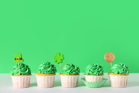 Tasty cupcakes for St. Patrick's Day on white table against green backgroundの写真素材