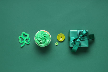 Tasty cupcake with gift box and decor for St. Patrick's Day on green backgroundの写真素材