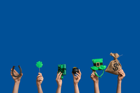Female hands holding gift box and party decor for St. Patrick's Day celebration on blue background...