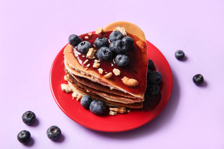 Plate with tasty pancakes in the shape of heart, blueberry and jam on purple background. Valentine's...