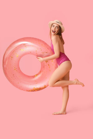 Happy young woman in tank swimsuit and with inflatable ring on pink backgroundの写真素材