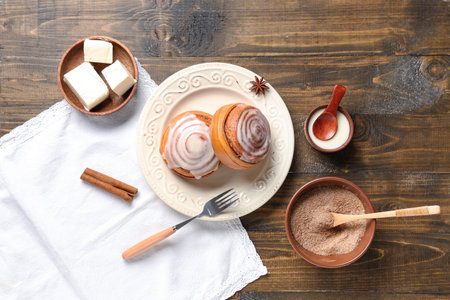 Plate with cinnamon buns and ingredients on wooden backgroundの写真素材