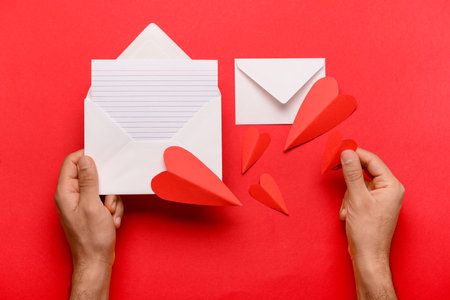Male hands with envelopes, blank card and paper hearts on red background. Valentine's Day celebrationの写真素材
