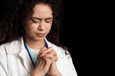 Female African-American medical intern praying on black background, closeupの写真素材