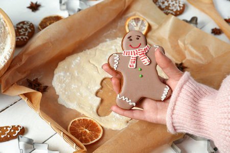 Female hand with sweet Christmas cookie and raw dough on light wooden background, closeup