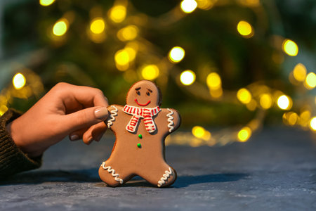 Female hand with sweet Christmas cookie on table against blurred lights