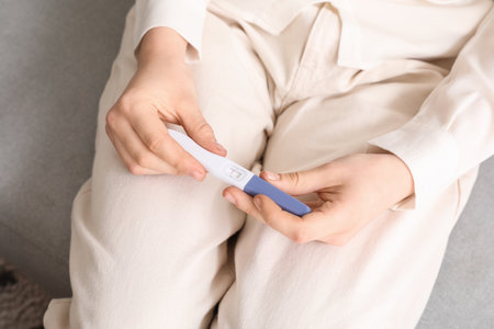 Woman with pregnancy test sitting on sofa at home, closeupの写真素材