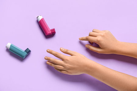 Child's hands with asthma inhalers on lilac background