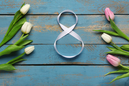 Figure 8 made of ribbon and tulip flowers on blue wooden background. International Women's Day celebrationの写真素材