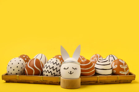 Wicker trays and wooden holder with painted Easter eggs on yellow backgroundの写真素材