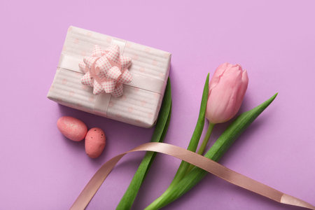 Easter eggs with tulip flower and gift box on purple background
