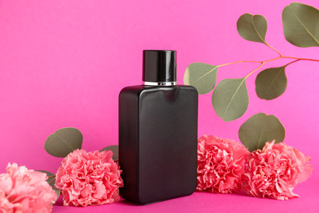 Black bottle of perfume with flowers and leaves on pink backgroundの写真素材