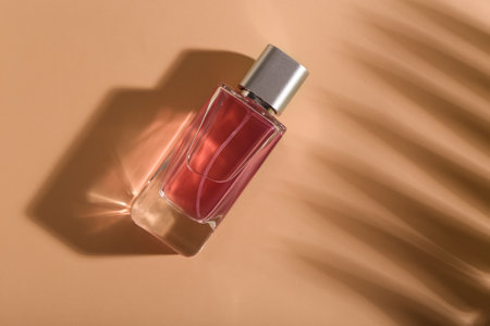Pink bottle of perfume with shade of palm branch on beige background. Top viewの写真素材