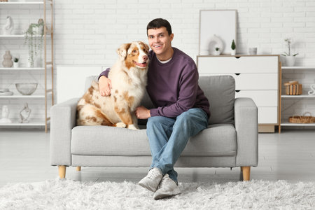 Young man with Australian Shepherd dog sitting on sofa at homeの写真素材