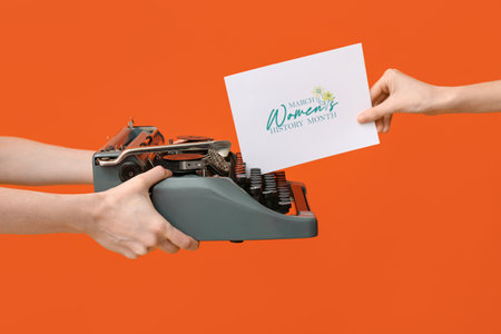 Female hands with retro typewriter and greeting card for International Women's Day on color background, closeupの写真素材