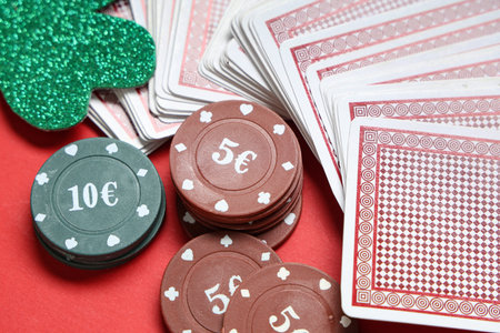 Poker chips with cards and lucky clover on red background, closeup. St. Patrick's Day celebration