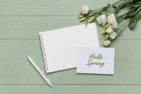 Greeting card with text HELLO SPRING, notebook and beautiful white eustoma flowers on green wooden...