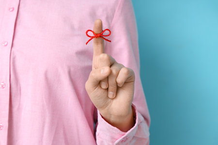 Woman with red bow on index finger against blue background. Reminder conceptの写真素材