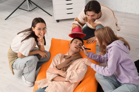 Young people drawing mustache on their sleeping colleague's face in office. April Fools' Day...