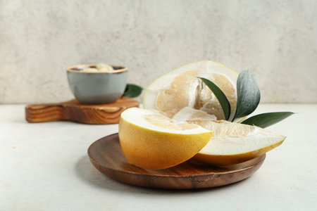 Wooden plate with cut fresh pomelo fruit and leaves on white background