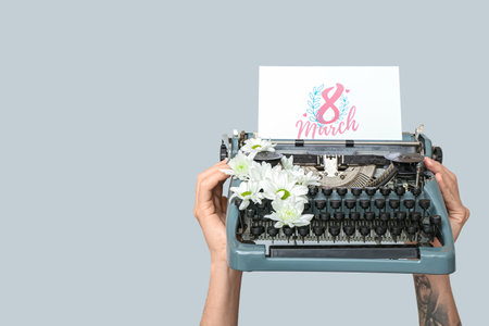 Hands holding vintage typewriter, flowers and festive postcard with text 8 MARCH on gray background. Women's Day celebrationの写真素材