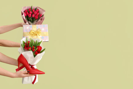 Female hands with bouquets of tulips, gift box and high heel shoe on green background. Shopping for International Women's Dayの写真素材