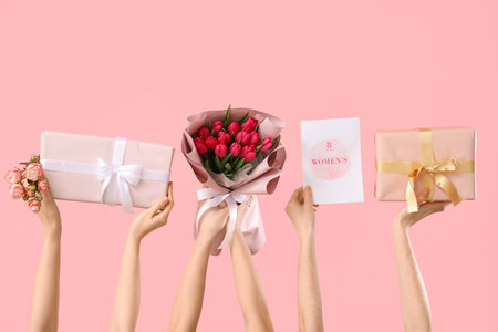 Female hands with bouquet of tulips, gift boxes and festive postcard on pink background. Shopping for International Women's Dayの写真素材