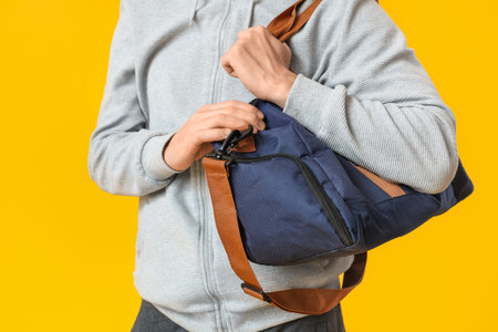 Young man with sports bag on yellow background