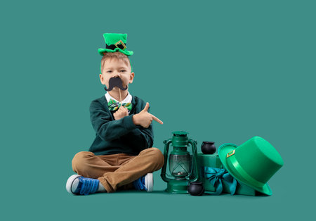 Cute little boy in festive outfit pointing at decorations for St. Patrick's Day celebration on green backgroundの写真素材