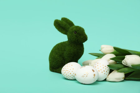 Bunny figurine with Easter eggs and tulips on turquoise background
