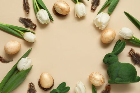 Frame made of Easter eggs with tulips, bunny figurine and feathers on beige background
