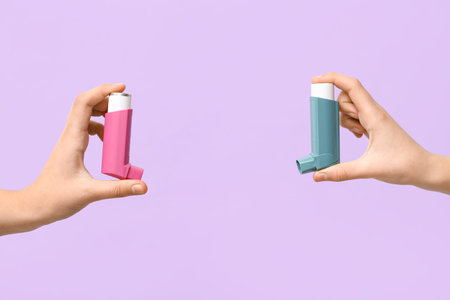 Child's hands with asthma inhalers on lilac background