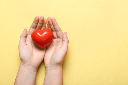 Female hands with red heart on yellow backgroundの写真素材