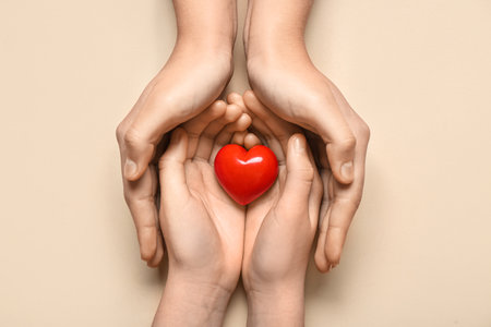 Hands of woman and child with red heart on beige backgroundの写真素材
