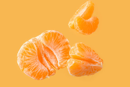 Flying sweet peeled mandarin on yellow backgroundの写真素材